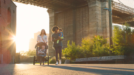 Family Day Out In New York City With Two Mums Walking By Brooklyn Bridge With Childrenの写真素材