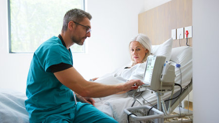 Male Nurse Taking Mature Female Patients Blood Pressure In Hospital Bed With Automated Machineの写真素材