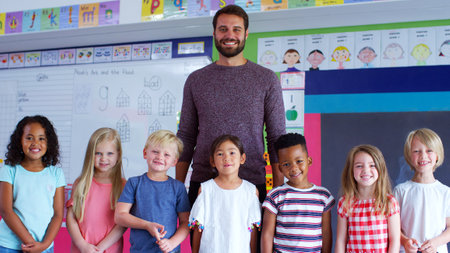 Portrait Of Multi-Cultural Elementary School Pupils Standing In Classroom With Male Teacherの写真素材
