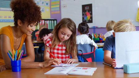 Female Elementary School Teacher Giving Female Pupil One To One Support In Classroom