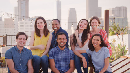 Portrait Of Friends Gathered On Rooftop Terrace For Party With City Skyline In Background