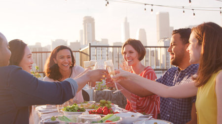 Friends Making Toast Gathered On Rooftop Terrace For Meal With City Skyline In Backgroundの写真素材