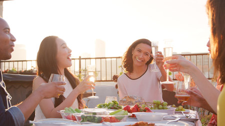 Friends Making Toast Gathered On Rooftop Terrace For Meal With City Skyline In Backgroundの写真素材