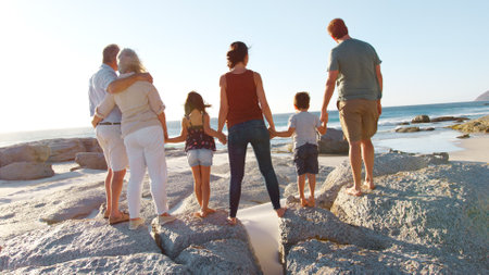 Rear View Of Multi-Generation Family On Summer Vacation Standing On Rocks Looking Out To Seaの写真素材