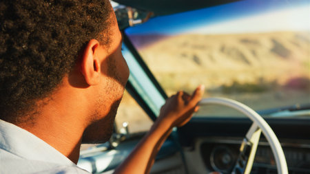 Close Up Of Man Driving Classic Open Top Car On Road Trip Through Countryside At Sunset