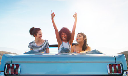 Three Female Friends In Back Seat Of Classic Open Top Car On Road Trip Through Countrysideの写真素材