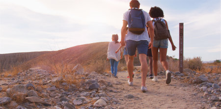 Rear View Of Multi-Cultural Group Of Friends Wearing Backpacks Hiking Through Countryside Together