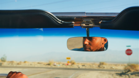 Male Driver Reflected In Mirror Driving Classic Open Top Car On Road Trip Through Countryside