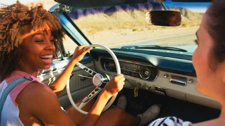 Close Up Of Two Female Friends Driving Classic Open Top Car On Road Trip In Countryside At Sunsetの写真素材