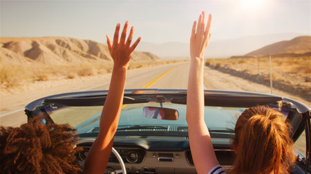 Two Female Friends Driving Classic Open Top Car On Road Trip In Countryside With Hands In The Airの写真素材