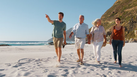 Senior Parents With Adult Offspring Walking Along Sandy Beach On Summer Vacationの写真素材