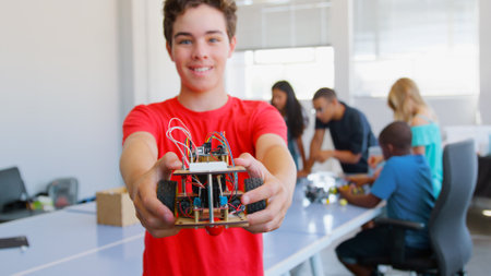 Portrait Of Smiling Male Student Holding Robot Vehicle Built In School Computer Coding Class