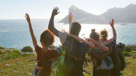 Rear View Of Group Of Young Friends Hiking Standing On Cliffs By Coast And Looking At Beautiful Viewの写真素材