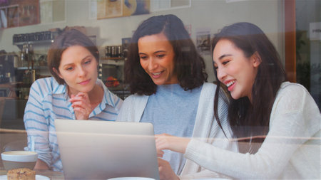 View Through Window Of Group Of Businesswomen Working At Laptop In Coffee Shopの写真素材