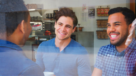 View Through Window Of Smiling Group Of Male Friends Meeting In Coffee Shop