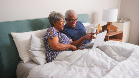 Senior Couple At Home Lying In Bed Having Video Call With Relatives On Laptopの写真素材