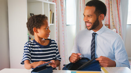 Father Helping Son To Pack Bag For School In Bedroom At Home