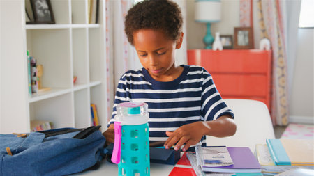 Young Boy Packing Bag For School In Bedroom At Home