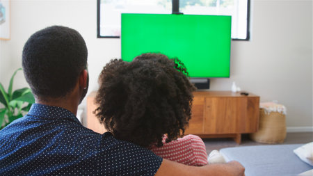 Rear View Of Hugging Couple Sitting On Sofa At Home Watching Green Screen TV Togetherの写真素材
