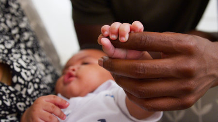 Close Up Of Baby Son Gripping Father's Finger As He Cuddles Him In Nursery At Home