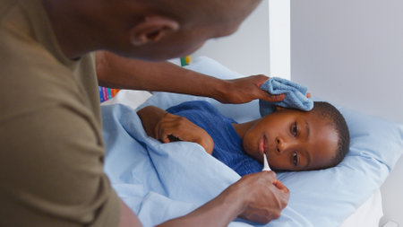 Father Caring For Sick Son Ill In Bed At Home Taking Temperature With Thermometerの写真素材