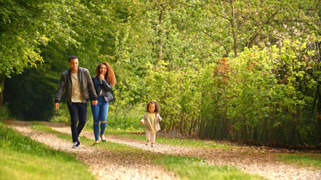 Family With Young Daughter Walking Along Track Through Trees In Countryside Towards Camera Togetherの写真素材