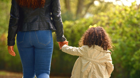 Rear View Of Mother Holding Daughter's Hand Walking Through Trees In Countryside Togetherの写真素材
