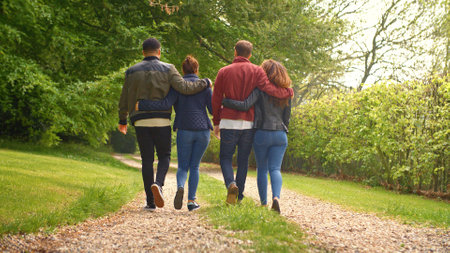 Rear View Of Group Of Young Friends Walking Along Track Through Trees In Countryside Togetherの写真素材