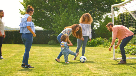 Group Of Friends Joining Family Outdoors In Park Or Garden Playing Football Togetherの写真素材