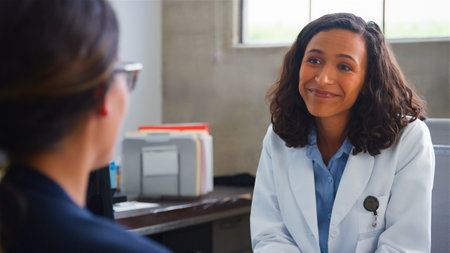 Female Patient Meeting With Doctor Wearing White Coat Sitting At Desk In Office Or Surgery