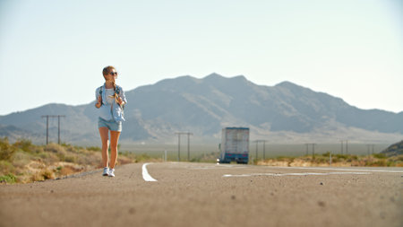 Young Woman With Backpack Hitchhiking Along Country Road Through Rocky Landscape