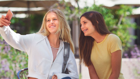 Two Female High School Students Posing For Selfie On Phone Outside College Or University Buildings