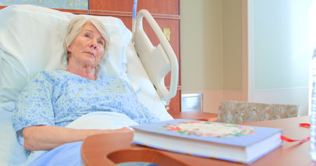 Unhappy Senior Female Patient Lying In Hospital Bed In Geriatric Wardの写真素材
