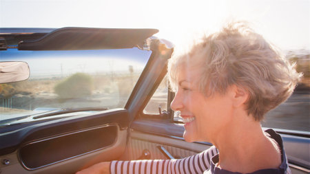Senior Woman Passenger On Road Trip Driving In Classic Convertible Car Along Country Roadの写真素材