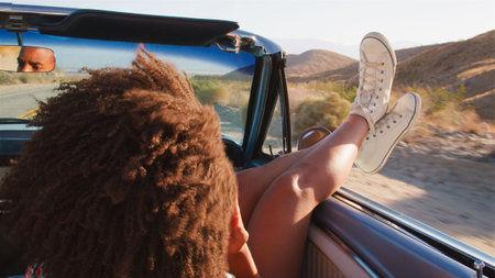 Woman Passenger With Feet Out Of Window On Road Trip Driving In Classic Convertible Car Along Road