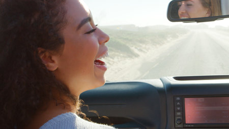 Close Up Of Two Young Female Friends On Road Trip Driving In Convertible Car On Country Road