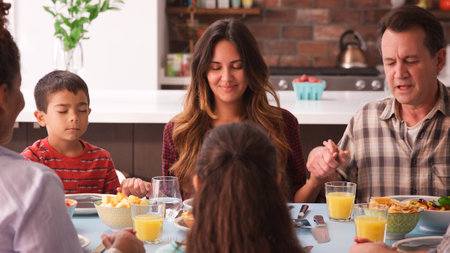 Multi Generation Family Praying Before Meal Around Table At Home
