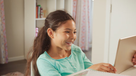 Smiling Young Girl Sitting At Desk In Bedroom At Home Using Digital Tablet