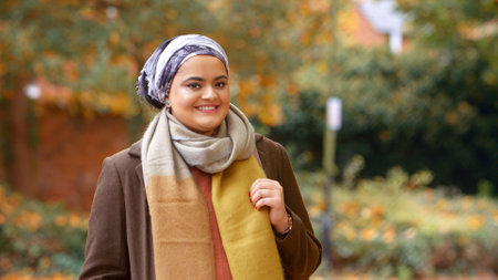 Portrait Of Smiling Young British Muslim Woman Wearing Headscarf In Autumn Park