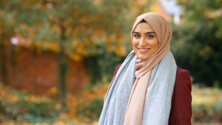 Head And Shoulders Portrait Of Smiling Young British Muslim Woman Wearing Hijab In Autumn Parkの写真素材