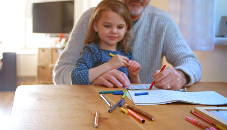 Grandfather And Granddaughter Sitting At Table At Home Colouring Picture Together