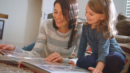 Mother And Daughter Lying On Floor At Home Talking And Looking Through Photo Album Togetherの写真素材