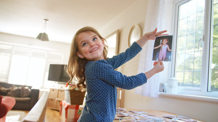 Smiling Young Girl Holding Up Family Photograph Of Herself From Table At Homeの写真素材