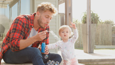 Father Having Fun Playing With Daughter Outside As She Blows Bubbles