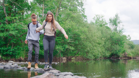 Young Couple Crossing River On Stepping Stones Hiking In UK Lake Districtの写真素材