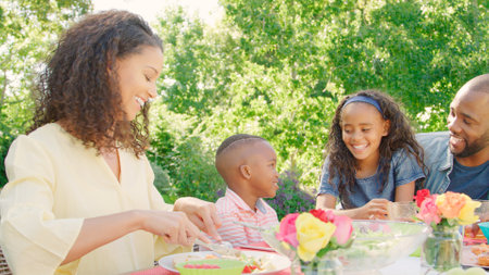 Family Sitting Around Outdoor Table In Summer Garden Enjoying Meal Together