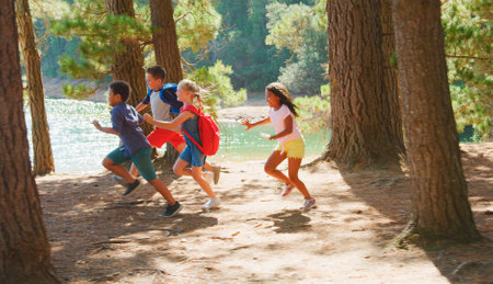 Group Of Children Running Along Trail By Lake On Hiking Adventure In Countryside