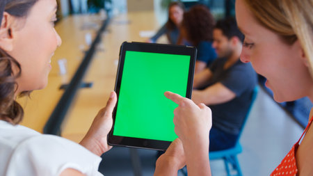 Close Up Of Two Businesswomen Looking At Digital Tablet With Green Screen In Shared Office