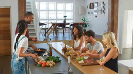 Couple Talking To Guests Whilst Making Food For Dinner Party At Home In Modern Kitchenの写真素材