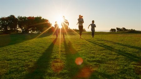 Low Angle Shot Of Family Running Towards Camera Across Field With Lens Flareの写真素材